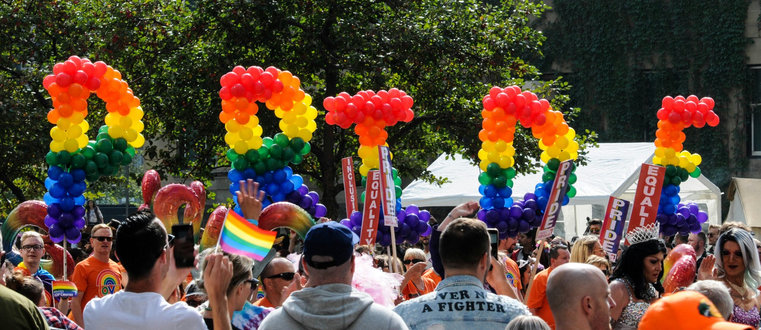 People in a crowd holding up rainbow balloons spelling out "PRIDE"