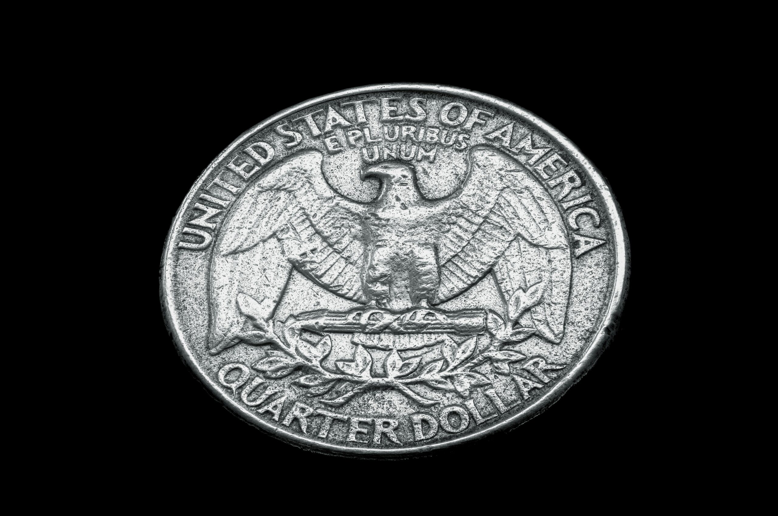 The eagle side of a US quarter dollar coin face up against a dark background